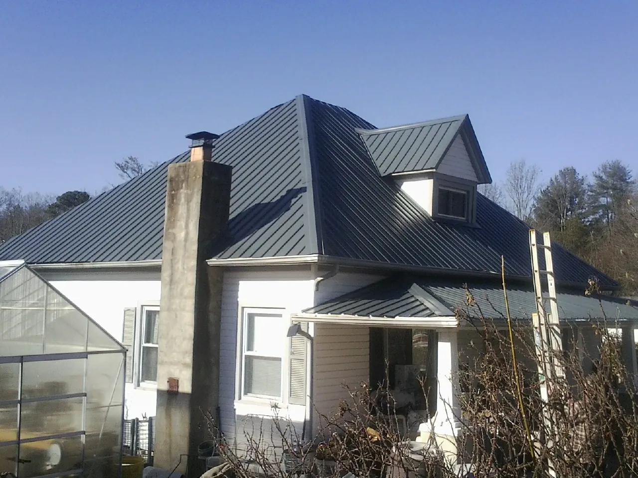 Dark blue standing seam metal roof on a white farmhouse with dormer — Slate & Tile Roof Repair by Roofing Brothers in Estes Park