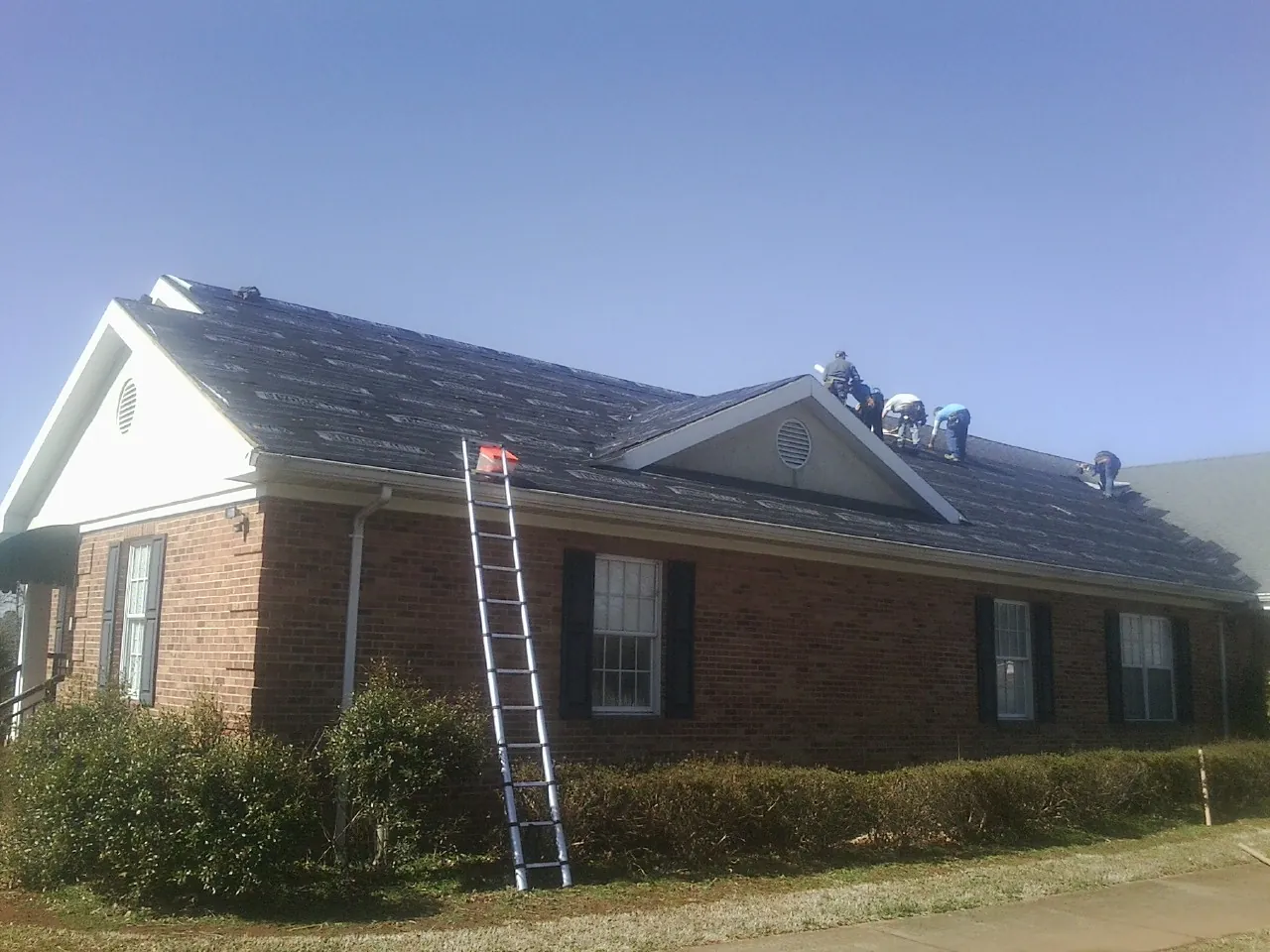 Crew tearing shingles off a brick ranch roof with a ladder set — Metal Roof Repair work by our crew in Estes Park
