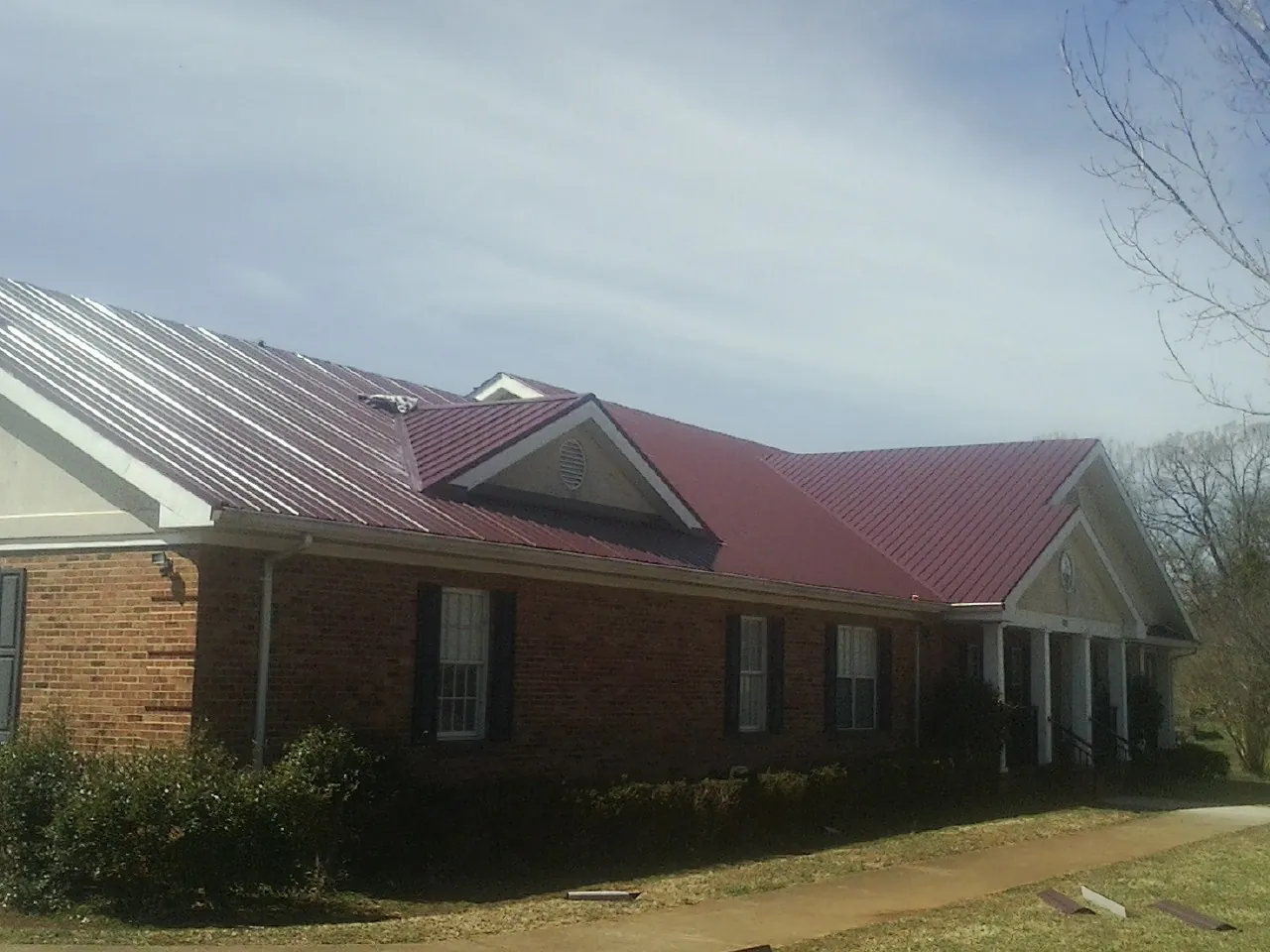 Red metal roof with gabled entries on a long brick building, from a Hail Damage Roof Repair job in Estes Park