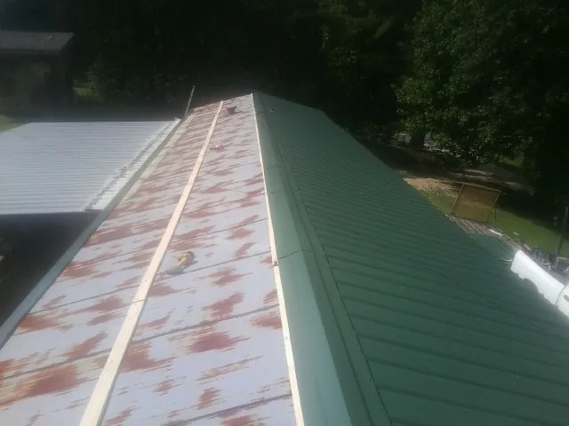 Old rusted panels beside newly installed green metal roofing — Wind Damage Roof Repair by Roofing Brothers in Estes Park
