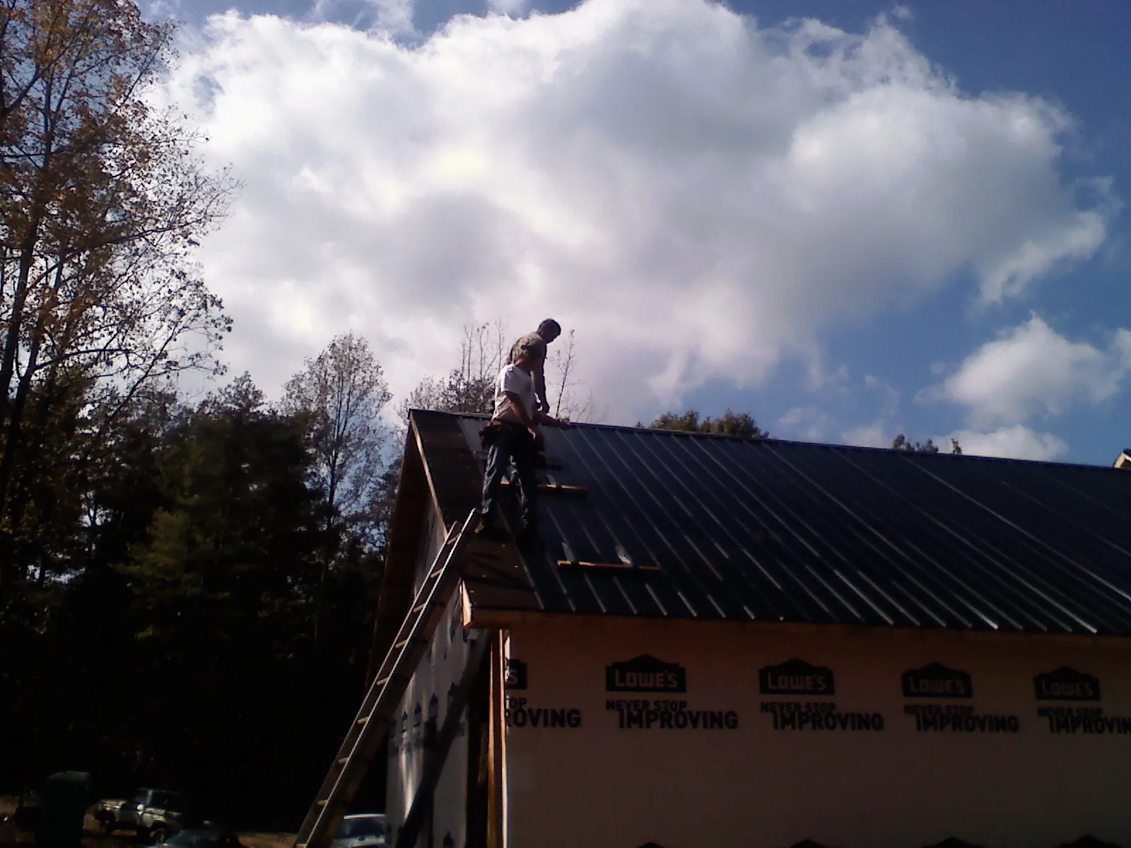 Roofer fastening dark metal panels high against a cloudy sky, from a Roof Inspection job in Estes Park